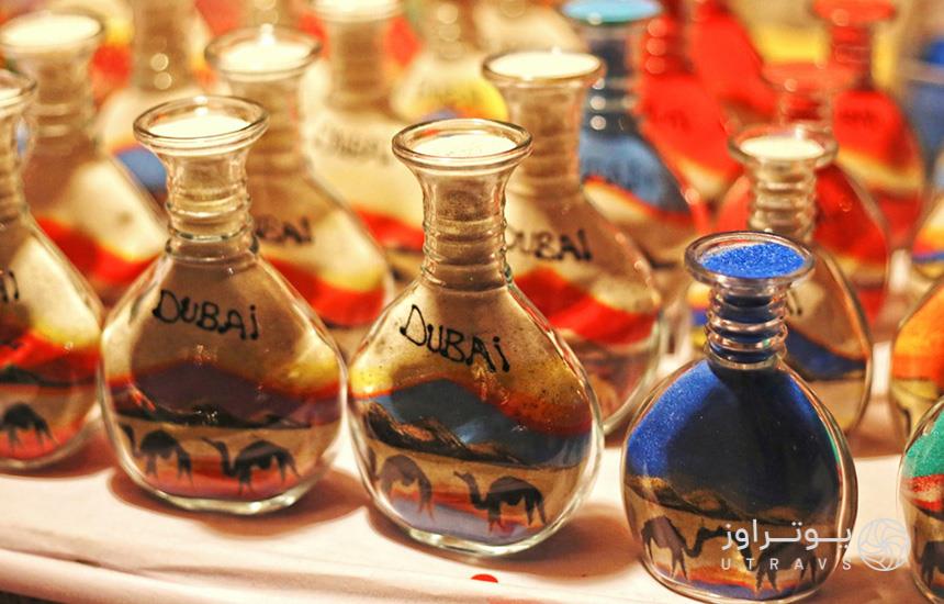 سوغات دبی؛ تصویری از چند شیشه‌ی پُر شده با شن‌های رنگی که واژه‌ی «Dubai» روی‌شان نوشته شده.